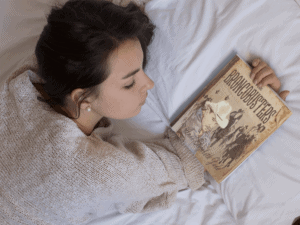 young girl holding a book on her hand while lying down on her bed mockup a14275